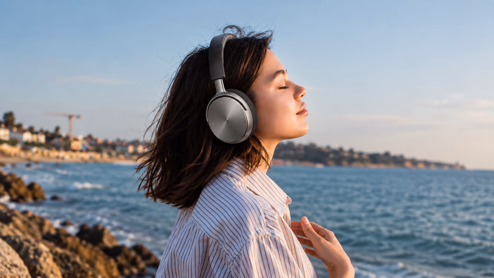 A woman with eyes closed wearing Sonicra headphones by the sea